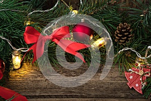 Christmas composition with pine branches, red toys and bows and a burning garland on a natural wooden background.