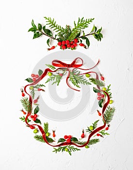 Christmas composition  with red ribbon, branches of spruce and holly with red berries in shape of Christmas bauble on white