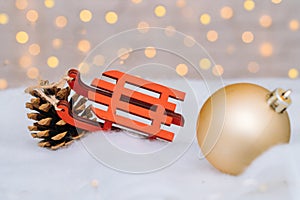 Christmas composition with red wooden Santa Claus sleigh, fir cone and Xmas tree balls over blurred light background