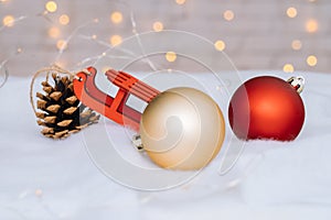 Christmas composition with red wooden Santa Claus sleigh, fir cone and Xmas tree balls over blurred light background