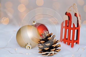 Christmas composition with red wooden Santa Claus sleigh, fir cone and Xmas tree balls over blurred light background