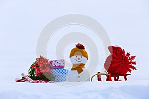 Christmas composition with snowy background. Snowman with red bag with the snowflake on the sledge. Colorful gift box.