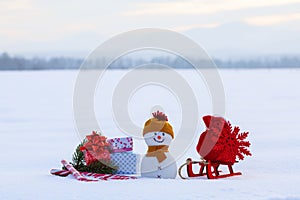 Christmas composition with snowy background. Snowman with red bag with the snowflake on the sledge. Colorful gift box.