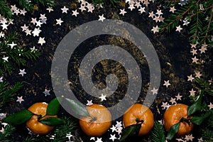 Christmas composition with tangerines on black background, with green spruce tree branch and stars. Flat lay