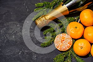 Christmas composition with tangerines and champagne on black background, with green spruce tree branch. Flat lay