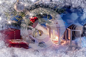 Christmas composition - a tree in the snow, gifts, decoration and a hand lighting a lantern with a match