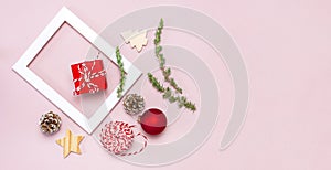 Christmas composition. White photo frame, fir branches, cones, red ball, twine, gift, wooden toys on pink background Flat lay top