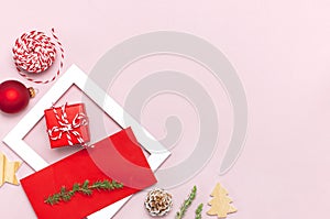 Christmas composition. White photo frame, red envelope, fir branches, cones, ball, twine, gift, wooden toys on pink background