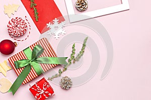 Christmas composition. White photo frame, red envelope, fir branches, cones, ball, twine, gift, wooden toys on pink background