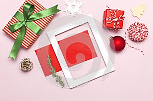 Christmas composition. White photo frame, red envelope, fir branches, cones, ball, twine, gift, wooden toys on pink background