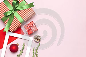 Christmas composition. White photo frame, red envelope, fir branches, cones, ball, twine, gift, wooden toys on pink background