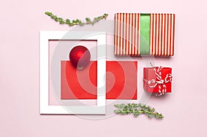 Christmas composition. White photo frame, red envelope, fir branches, cones, ball, twine, gift, wooden toys on pink background