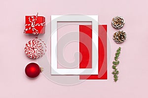 Christmas composition. White photo frame, red envelope, fir branches, cones, ball, twine, gift, wooden toys on pink background Fla