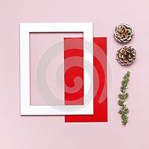 Christmas composition. White photo frame, red envelope, fir branches, cones, ball, twine, gift, wooden toys on pink background Fla