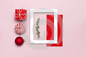 Christmas composition. White photo frame, red envelope, fir branches, cones, ball, twine, gift, wooden toys on pink background Fla