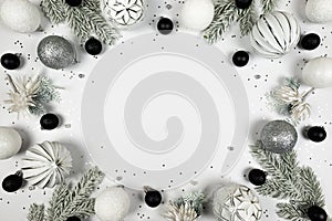 Christmas composition, white and silver decorations, black baubles, fir tree branches, silver stars confetti on white background.