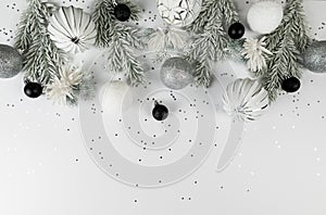 Christmas composition, white and silver decorations, black baubles, fir tree branches, silver stars confetti on white background.