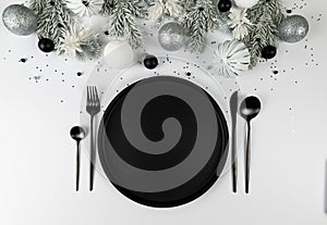 Christmas composition, white and silver decorations, black plate and cutlery, fir tree branches on white background.