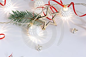 Christmas composition of wooden stars, a garland of white luminous balls, fir branches, bells and a red ribbon on a white