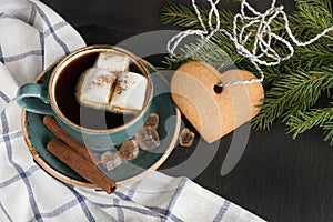 Christmas concept. Blue mug of hot coffee with marshmallow and cookies on a black background with Christmas tree branches. Top vie