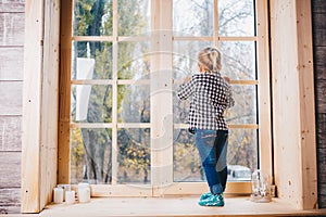 Christmas concept. A child with blonde hair in warm socks, jeans and shirt is standing with her back on the windowstick, putting h