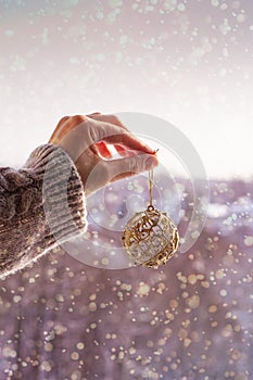 Christmas concept with hand and golden ball - christmas tree toy. Christmas decoration on snow background