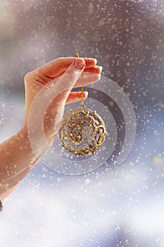 Christmas concept with hand and golden ball - christmas tree toy. Christmas decoration on snow background