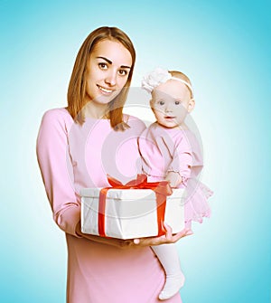 Christmas concept - happy smiling mother and baby in pink dress with box gift