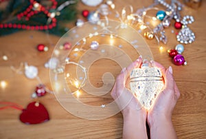 Christmas concept. Human hands hold a ceramic christmas decoration in a shape of glowing heart