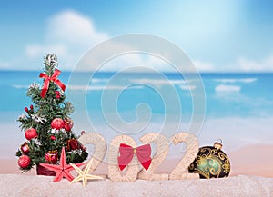 Christmas concept. New year 2022 sign with Christmas tree and a large ball on beach background