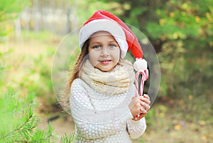 Christmas concept - portrait little girl child in santa red hat with sweet lollipop cane