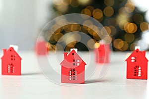 Christmas concept with red houses on white wooden table on blurred lights background