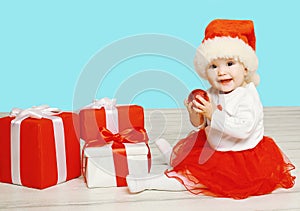 Christmas concept - smiling child in santa red hat with boxes gifts sitting on floor