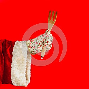Christmas cooking and tasting. Festive meals concept. Santa Claus`s hand in a kitchen glove holds a wooden fork