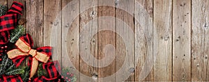 Christmas corner border banner with red and black checked buffalo plaid ribbon, burlap and branches, top view on a wood background