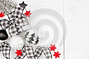 Christmas corner border of black and white checked buffalo plaid ribbon, gifts and ornaments, overhead on a white wood background