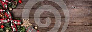 Christmas corner border of ornaments, branches and red and green plaid  ribbon on a rustic wood banner background