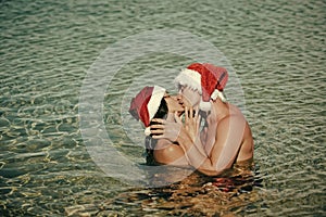 Christmas couple in love kiss as santa in beach water