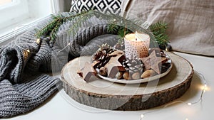 Christmas cozy calm scene. Burning candle standing near window. Glittering Christmas lights. Natural decoration of pine