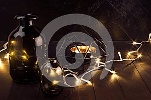 Christmas cozy dark modern interior - back and golden decoration - twinkle warm garland with elegant bottles on dark wood table.
