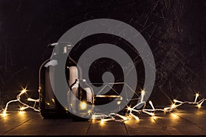 Christmas cozy dark modern interior - back and golden decoration - twinkle warm garland with elegant bottles on dark wood table.