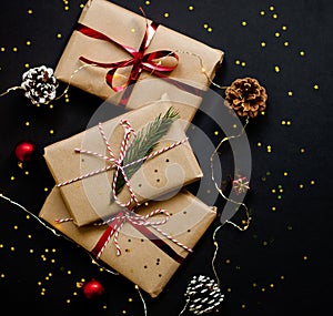 Christmas craft gift boxes with red ribbons, pine cones and red and golden decorations against black