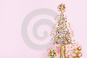 Christmas creative fir tree from champagne, confetti stars and serpentine with gift box on pink background top view. Flat lay.