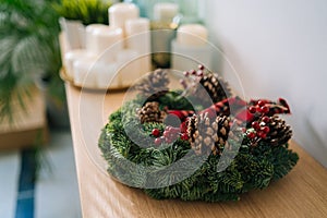 Christmas crown and winter wreath decoration with holly, fir, blue spruce, pine cones on wooden table