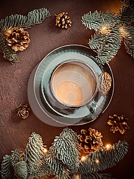 Christmas cup of coffee and fir branches with pine cones and garlands on brown background