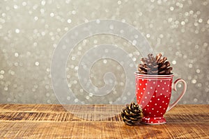 Christmas cup and pine corn decoration on wooden table over bokeh background