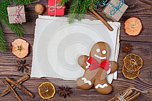 Christmas greeting card, old blank paper sheet, gingerbread man with frame made of fir, and spices, wooden background