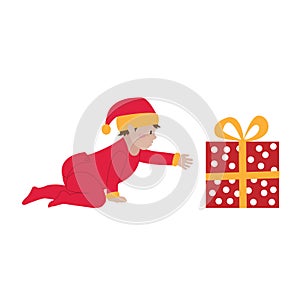 Christmas. A cute little baby in a red overalls and a santa claus hat is reaching for a Christmas present