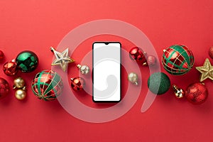 Christmas Day concept. Top view photo of smartphone star ornaments gold green and red baubles on isolated red background with