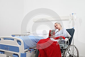 Christmas day isolated in hospital room with coronavirus, sad and pensive elderly woman on wheelchair with red hat and gift near